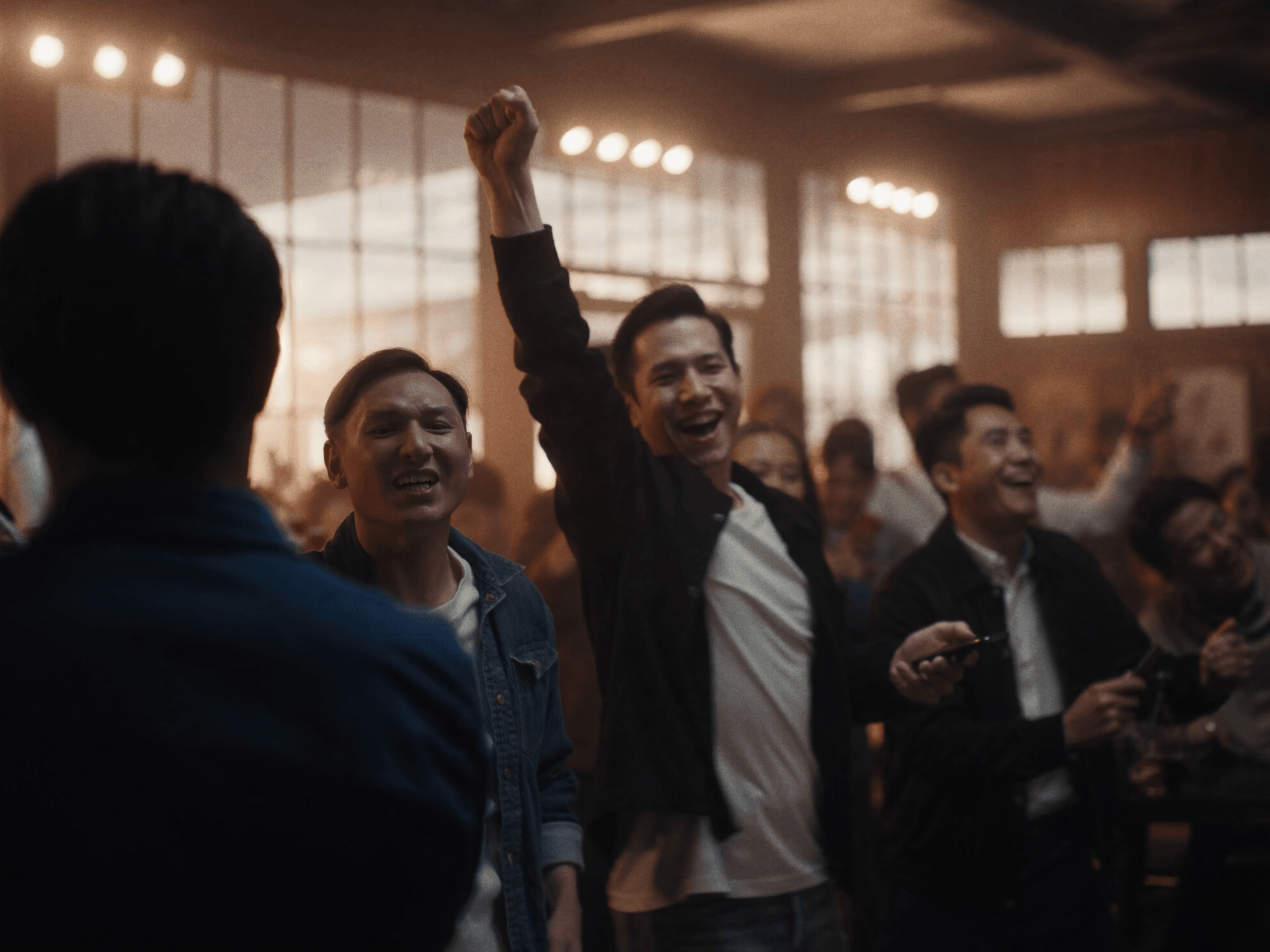 Friends cheering together in a warm, crowded room, one with a fist in the air