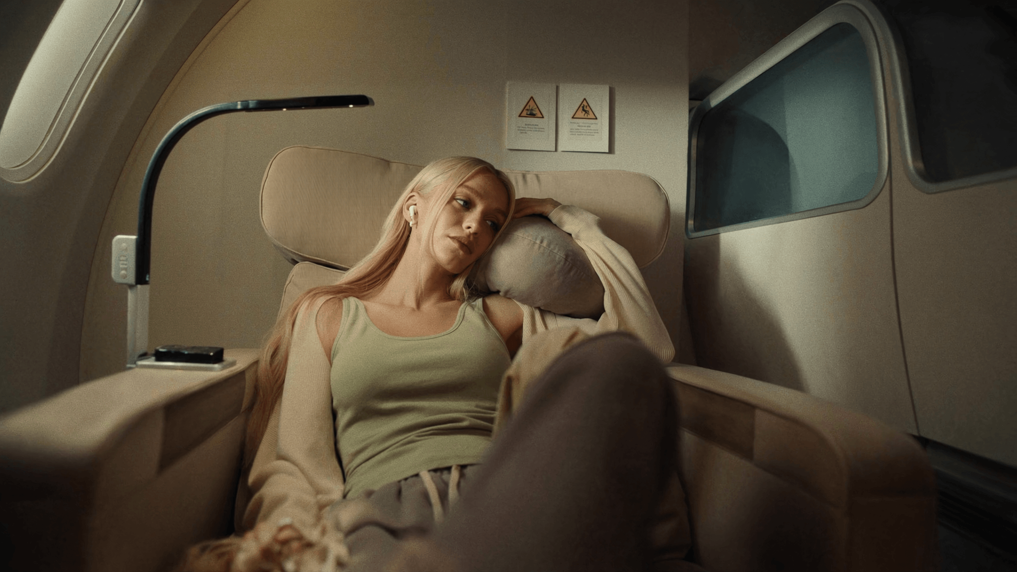 A traveler relaxing in a plane seat with earbuds in, head resting on a pillow